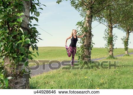 Stock Photograph - Mid adult female runner stretching legs in park. Fotosearch
