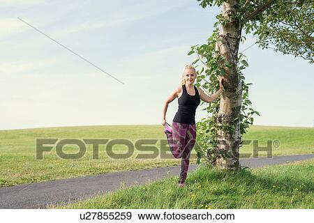Stock Photo - Mid adult female runner warming up in park. Fotosearch