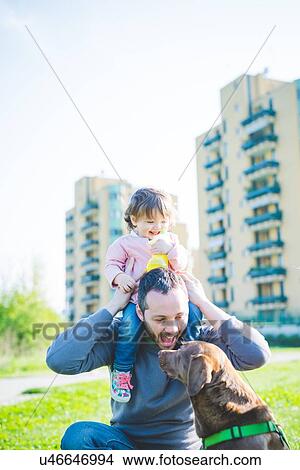 Picture - Mid adult man with toddler daughter on shoulders in park. Fotosearch