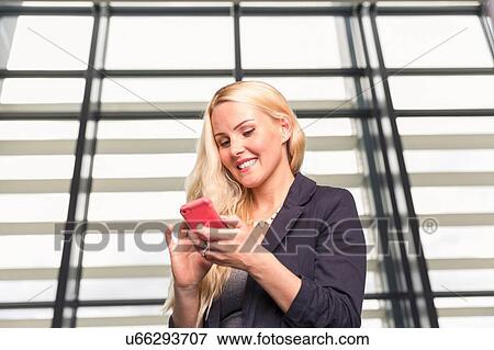 Stock Photo - Mid adult woman checking smartphone, smiling. Fotosearch
