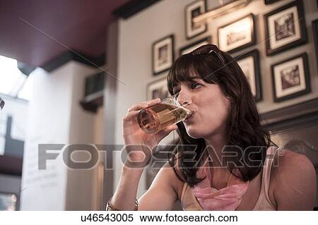 Stock Photography - Mid adult woman drinking beer in traditional pub. Fotosearch