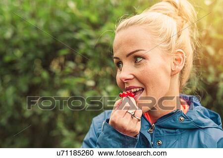 Stock Image - Mid adult woman eating redcurrants, outdoors. Fotosearch