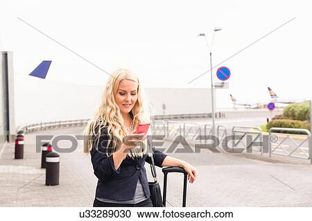 Mid adult woman outside airport, looking at cellphone View Large Photo Image Stock Image - Mid adult woman outside airport, looking at cellphone. Fotosearch