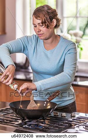 Mid adult woman pouring oil into wok at kitchen hob View Large Photo Image Stock Photo - Mid adult woman pouring oil into wok at kitchen hob. Fotosearch