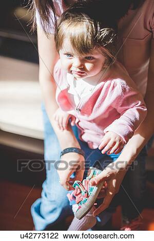 Stock Image - Mid adult woman putting on toddler daughters trainer shoe. Fotosearch