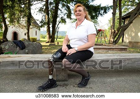 Stock Image - Mid adult woman with prosthetic leg, sitting on fence. Fotosearch