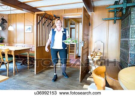 Stock Image - Mid adult woman with prosthetic leg, holding plates of food. Fotosearch