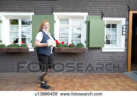 Stock Photo - Mid adult woman with prosthetic leg, carrying mugs, outdoors. Fotosearch