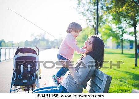 Stock Photo - Mid adult woman with toddler daughter on park bench. Fotosearch