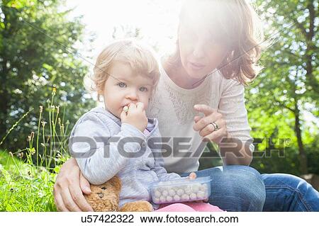 Mother and female toddler eating sweets in park View Large Photo Image Stock Image - Mother and female toddler eating sweets in park. Fotosearch