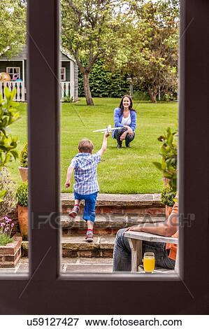 Stock Photo - Mother watching son play in garden with toy airplane. Fotosearch