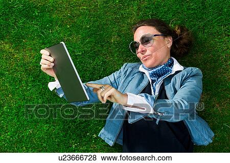Overhead view of mature woman lying on grass using touchscreen on digital tablet View Large Photo Image Stock Photo - Overhead view of mature woman lying on grass using touchscreen on digital tablet. Fotosearch