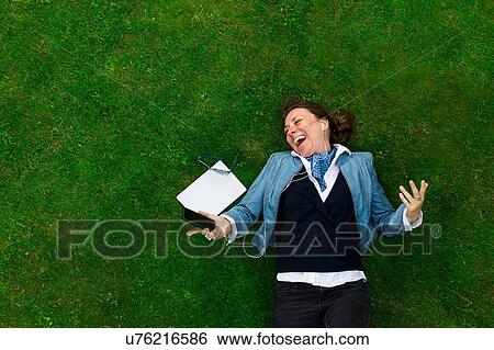 Overhead view of mature woman lying on grass laughing whilst listening to smartphone music View Large Photo Image Stock Photograph - Overhead view of mature woman lying on grass laughing whilst listening to smartphone music. Fotosearch