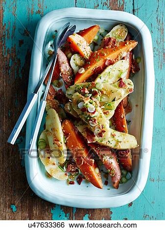 Stock Photograph - Overhead view of roasted vegetable dish with mustard seeds on rustic table. Fotosearch