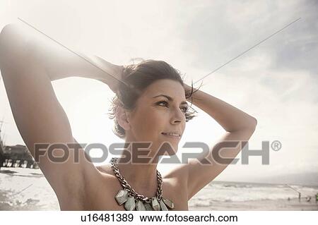 Portrait of beautiful young woman with hand in hair gazing out from beach View Large Photo Image Stock Photo - Portrait of beautiful young woman with hand in hair gazing out from beach. Fotosearch