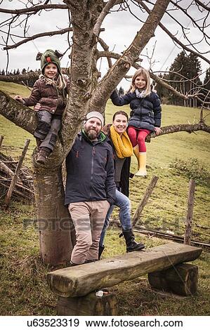 Stock Photo - Portrait of couple with two daughters climbing bare tree. Fotosearch