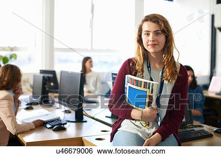 Stock Photograph - Portrait of female student holding file infront of computer class. Fotosearch