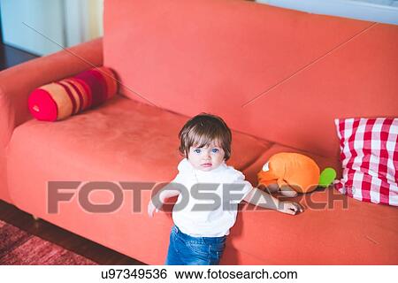 Stock Photograph - Portrait of female toddler leaning against sofa. Fotosearch