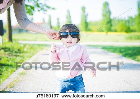 Stock Photo - Portrait of female toddler wearing sunglasses in park. Fotosearch