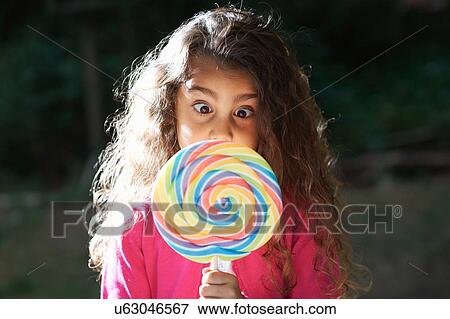 Portrait of girl crossing eyes with lollipop in front of her face in garden View Large Photo Image Stock Photo - Portrait of girl crossing eyes with lollipop in front of her face in garden. Fotosearch