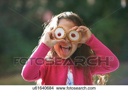 Picture - Portrait of girl with tartlets in front of her eyes in garden. Fotosearch