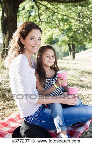 Portrait of mature woman and daughter drinking from paper cups at park picnic View Large Photo Image Stock Image - Portrait of mature woman and daughter drinking from paper cups at park picnic. Fotosearch