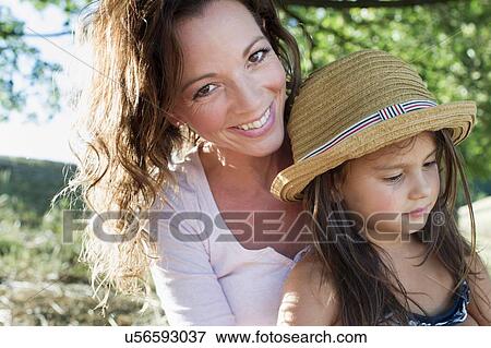 Stock Photo - Portrait of mature woman and daughter wearing straw hat in park. Fotosearch