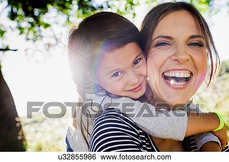 Portrait of mature woman giving daughter piggy back in sunlit park View Large Photo Image Stock Photograph - Portrait of mature woman giving daughter piggy back in sunlit park. Fotosearch