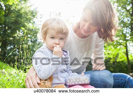 Portrait of mother and female toddler eating sweets in park View Large Photo Image Picture - Portrait of mother and female toddler eating sweets in park. Fotosearch