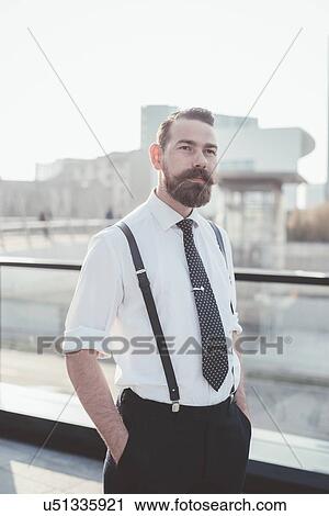 Stock Image - Portrait of stylish businessman with hands in pockets in city. Fotosearch