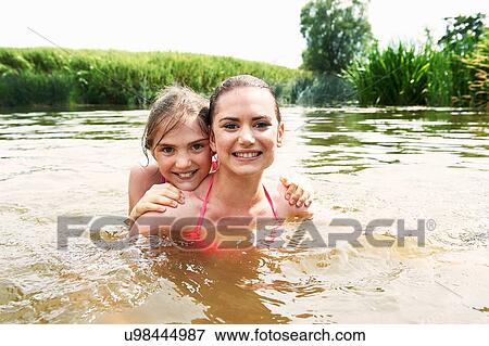 Stock Photo - Portrait of teenage girl and sister swimming in rural lake. Fotosearch