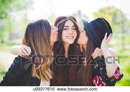 Portrait of three stylish young female friends kissing on cheek in park View Large Photo Image Stock Photography - Portrait of three stylish young female friends kissing on cheek in park. Fotosearch