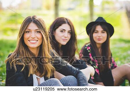 Stock Photography - Portrait of three young female friends sitting in park. Fotosearch