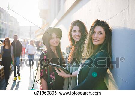 Stock Photography - Portrait of three young women using digital tablet on city street. Fotosearch