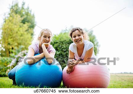 Stock Photography - Portrait of two tween girls on exercise balls in garden. Fotosearch