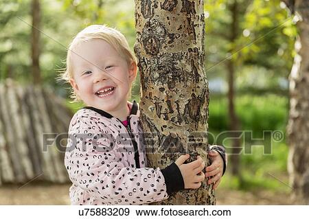 Portrait of young girl holding onto tree, smiling View Large Photo Image Stock Photo - Portrait of young girl holding onto tree, smiling. Fotosearch