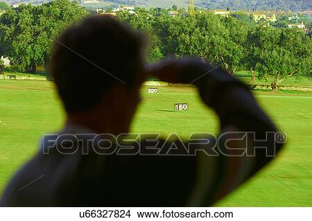 Rear view of mid adult man shielding eyes looking at golf course, focus on background View Large Photo Image Picture - Rear view of mid adult man shielding eyes looking at golf course, focus on background. Fotosearch