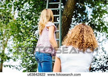 Stock Image - Rear view of two tween girls climbing tree ladder. Fotosearch