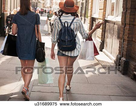 Stock Photography - Rear view of two women carrying shopping bags on city street. Fotosearch