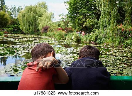 Stock Image - Rear view of two young brothers looking down from footbridge to lily pond. Fotosearch