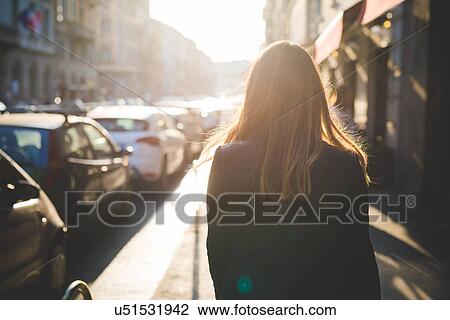 Rear view of young woman strolling on city street View Large Photo Image Stock Image - Rear view of young woman strolling on city street. Fotosearch