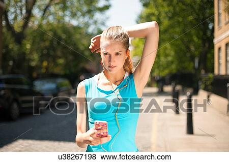 Stock Photo - Runner listening to music in smartphone on street, Wapping, London. Fotosearch