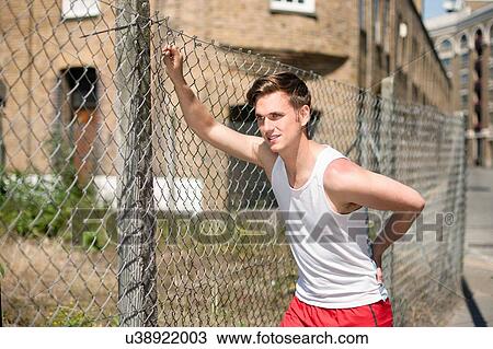Stock Image - Runner stretching against wire fence, Wapping, London. Fotosearch