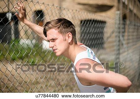 Stock Image - Runner stretching against wire fence, Wapping, London. Fotosearch