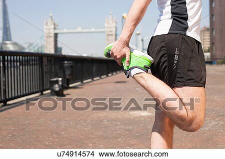 Picture - Runner stretching on riverfront, Wapping, London. Fotosearch