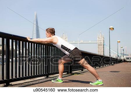 Stock Image - Runner stretching on riverfront, Wapping, London. Fotosearch