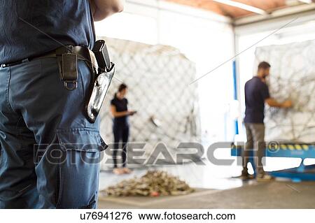 Stock Photograph - Security guard watching workers in air freight warehouse. Fotosearch