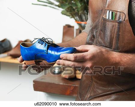 Stock Image - Shoemaker holding blue shoe in workshop. Fotosearch