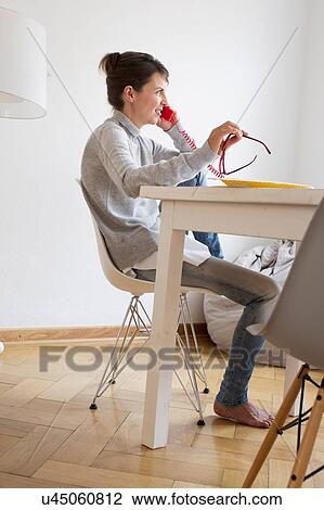 Side view of mature woman sitting at table talking on red landline telephone View Large Photo Image Stock Image - Side view of mature woman sitting at table talking on red landline telephone. Fotosearch