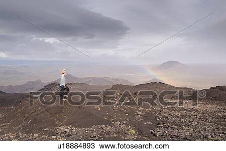 Stock Image - Side view of mid adult woman on volcanic landscape looking at rainbow, Helgafell, Iceland. Fotosearch